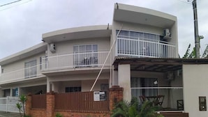 A two-story building with a balcony on the upper floor, a brick wall, and a small garden area. - Bela Catarina - Penha - Beto Carrero (Penha)