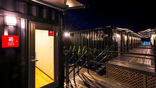 A corridor with a vending machine sign, a staircase, and a row of cabins with a sign reading "18-33 LOUNGY". - HOTEL R9 The Yard Ashikagafukutomi (Ashikaga)