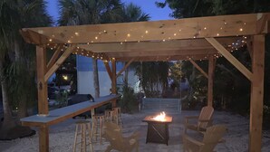 An outdoor patio with a wooden pergola, string lights, a fire pit, and seating arrangements. - WALK TO BEACH ACCESS! DOG FRIENDLY PROPERTY! (Englewood)
