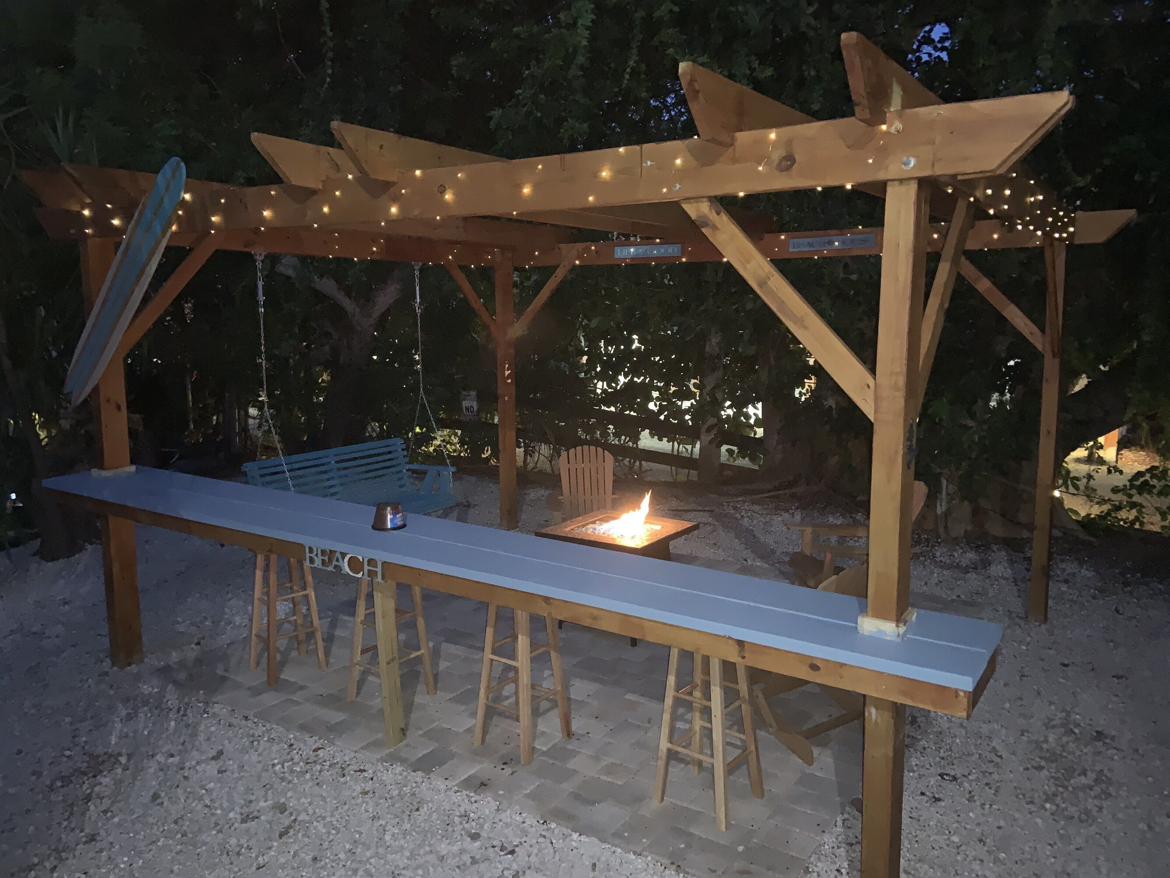 A wooden pergola with string lights, a bench, and a fire pit.