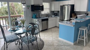 A modern kitchen with white cabinets, a blue accent wall, a stainless steel refrigerator, and a dining area with a glass table and chairs. - WALK TO BEACH ACCESS! DOG FRIENDLY PROPERTY! (Englewood)