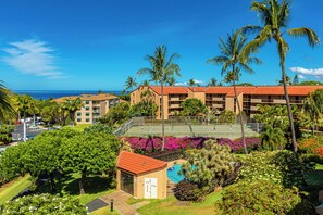 A hotel with multiple buildings, a tennis court, a swimming pool, and a view of the ocean.
