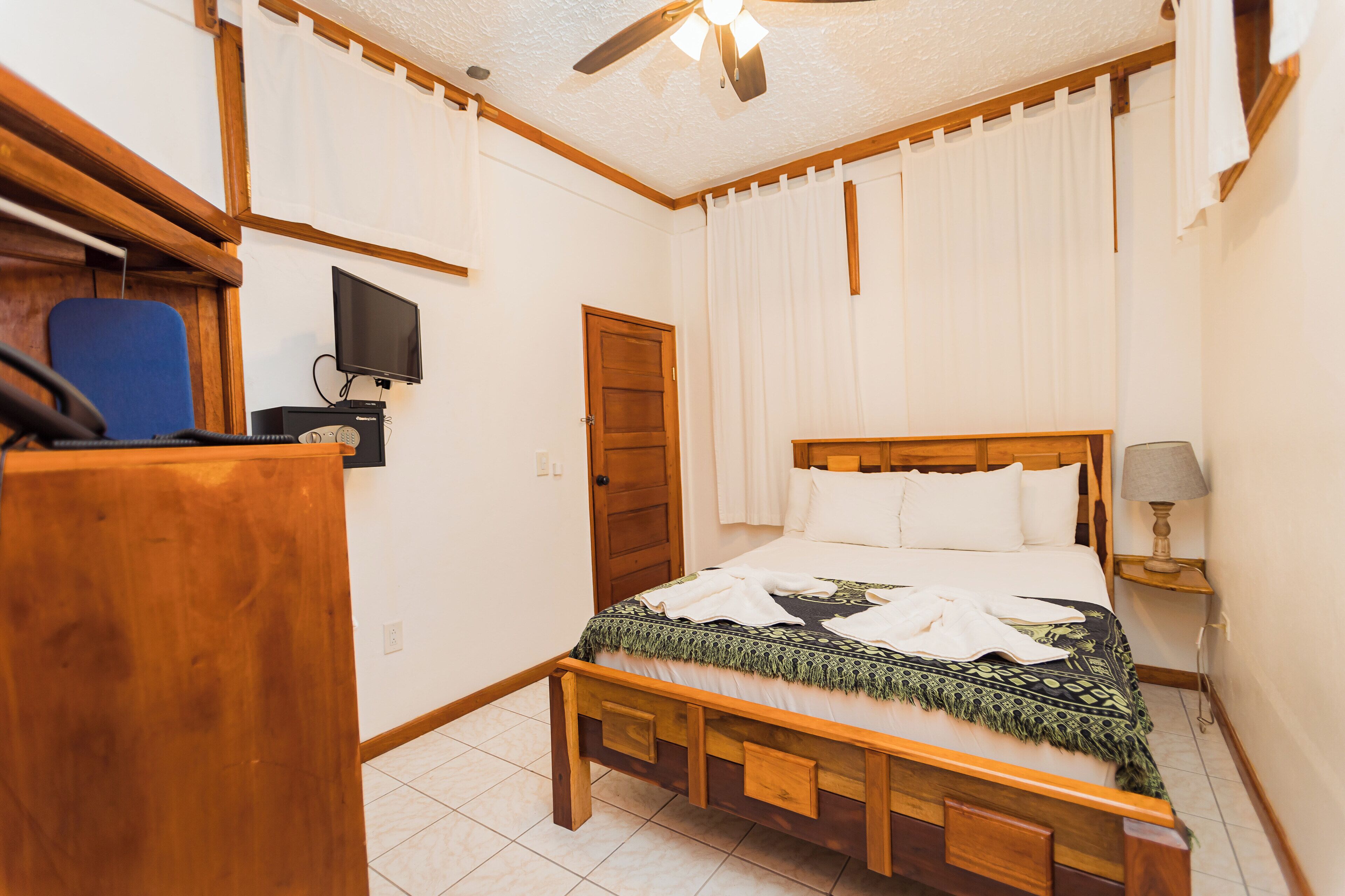 A bedroom with a wooden bed, a television, a desk, and a ceiling fan.