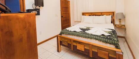 A bedroom with a wooden bed, a television, a desk, and a ceiling fan.