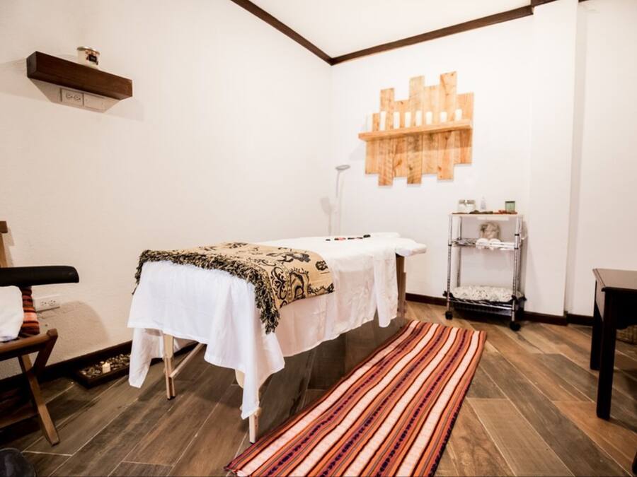 A room with a massage table, a wooden bench, a small shelf with items, and a patterned rug.