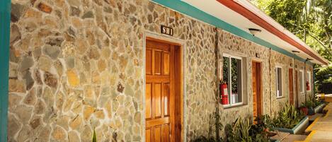 A stone building with a wooden door labeled "SH1," potted plants, and a red and white awning.