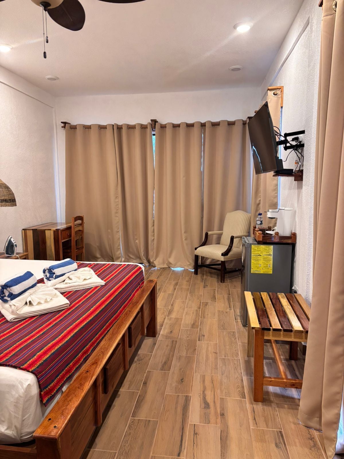 Una habitación de hotel con cama, escritorio, silla, televisor y ventana con cortinas.