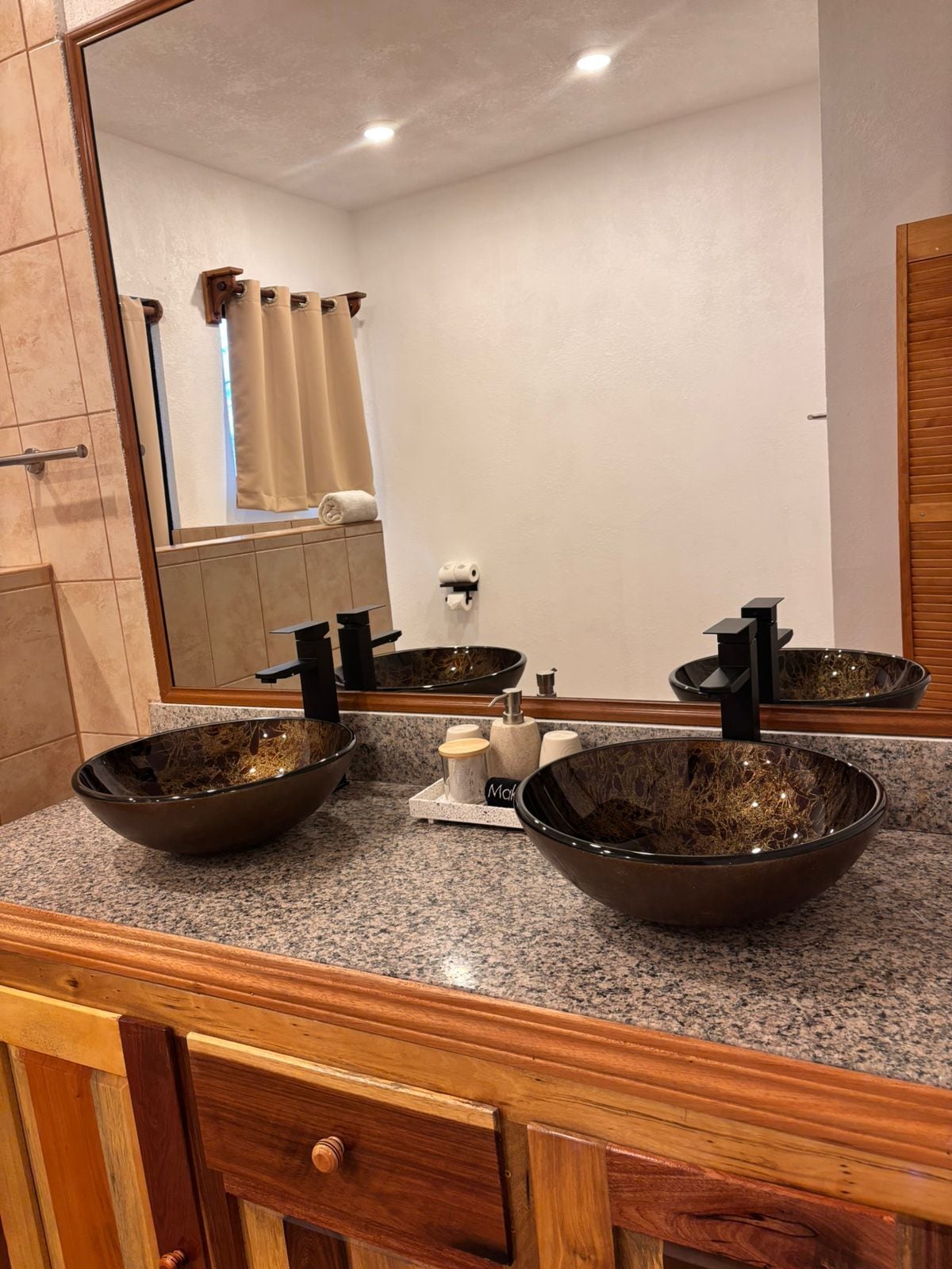 A bathroom with a granite countertop, two vessel sinks, a mirror, and a towel rack.
