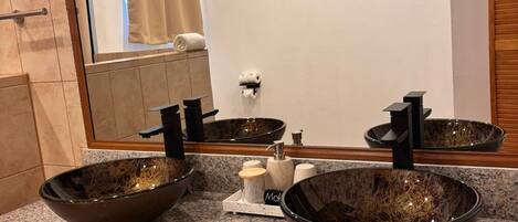A bathroom with a granite countertop, two vessel sinks, a mirror, and a towel rack.