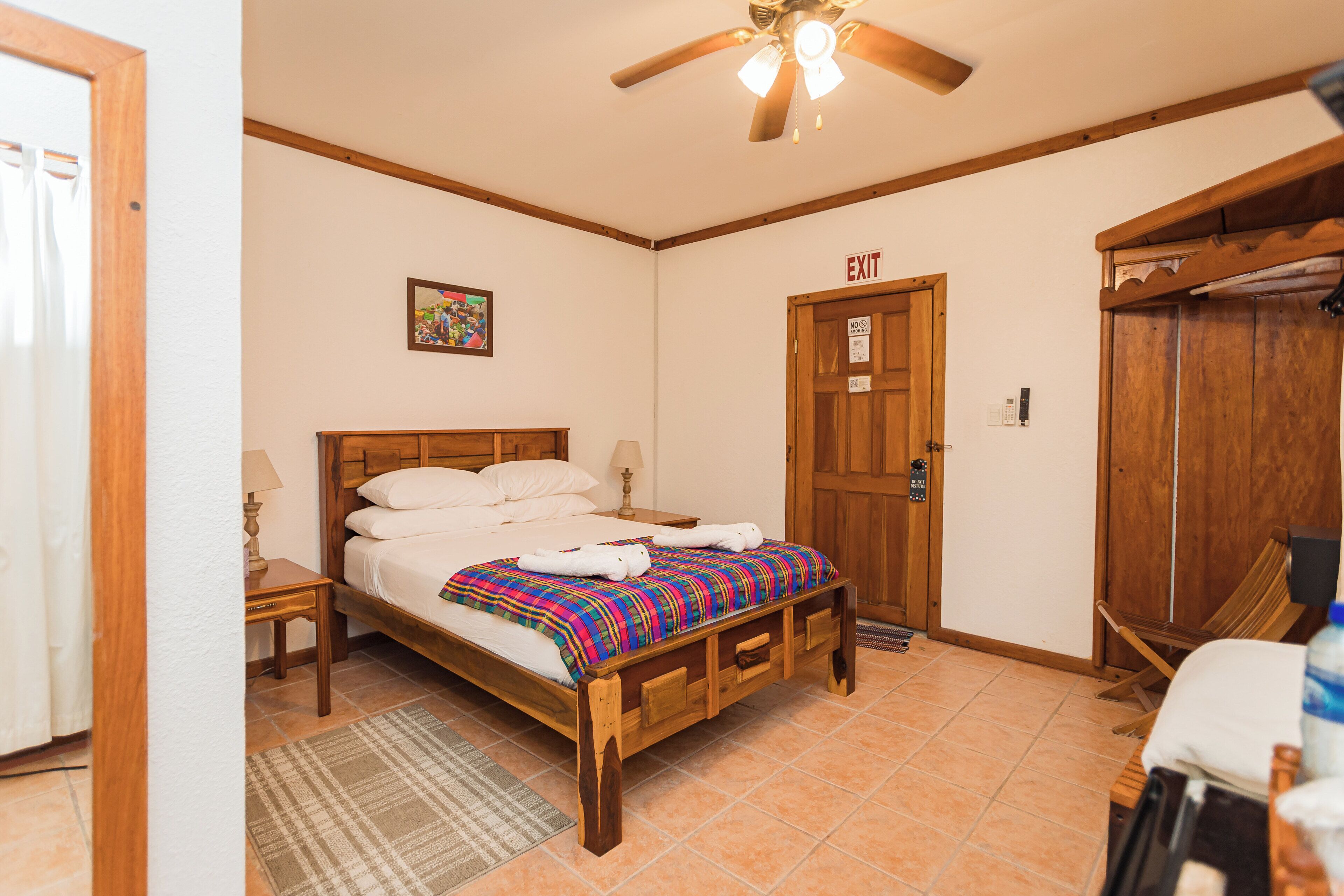 A bedroom with a wooden bed, a ceiling fan, an exit door, and a wooden wardrobe.