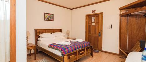 Un dormitorio con una cama de madera, un ventilador de techo, una puerta de salida y un armario de madera.