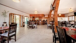 A spacious dining area with wooden paneling, multiple tables and chairs, and hanging pendant lights.