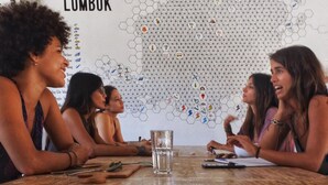 A group of people sitting around a wooden table in a room with a hexagonal wall design labeled "Lombok". - Kaniu Capsule Hostel (Kuta)