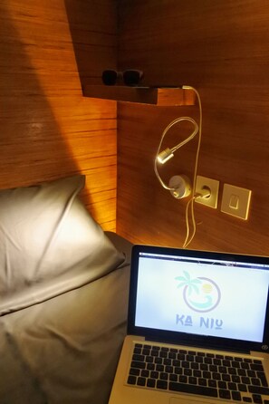 A laptop on a bed with a wooden headboard, a power outlet, and a wall socket.