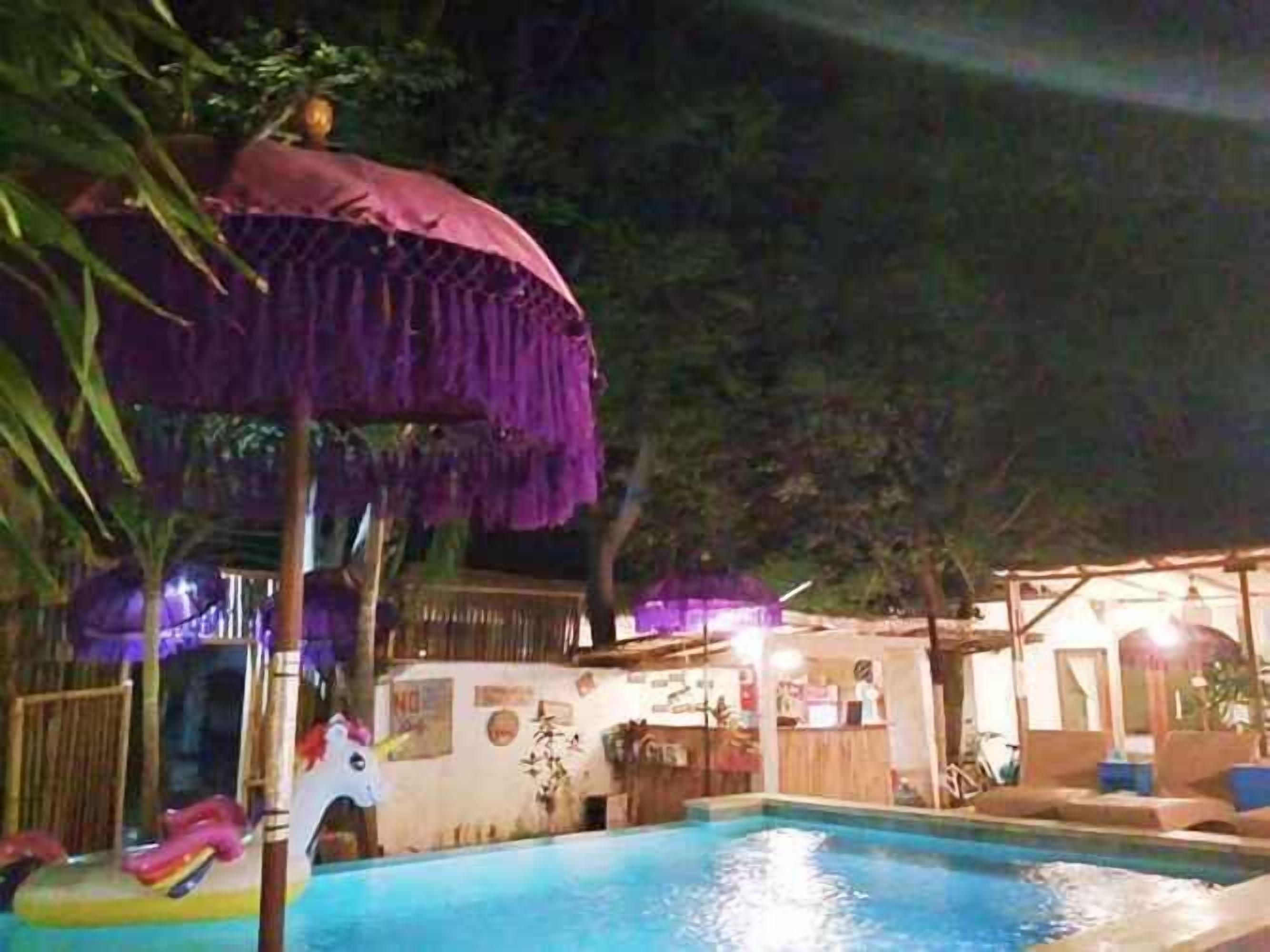 Una piscina con una estructura de techo de paja, un pequeño espacio de juegos con una figura de unicornio y una zona de bar con asientos.