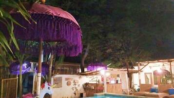 Una piscina con una estructura de techo de paja, un pequeño espacio de juegos con una figura de unicornio y una zona de bar con asientos.