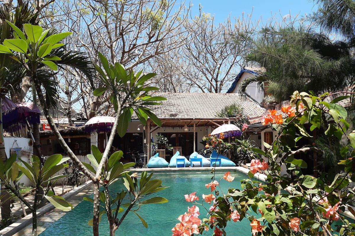 A pool area with clear water, surrounded by tropical plants and umbrellas.
