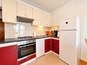 Een moderne keuken met een gasfornuis, oven, witte en rode kasten en een witte koelkast.
