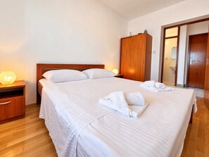 Een hotelkamer met een groot bed, een houten garderobe, nachtkastje en een badkamer zichtbaar door een geopende deur.