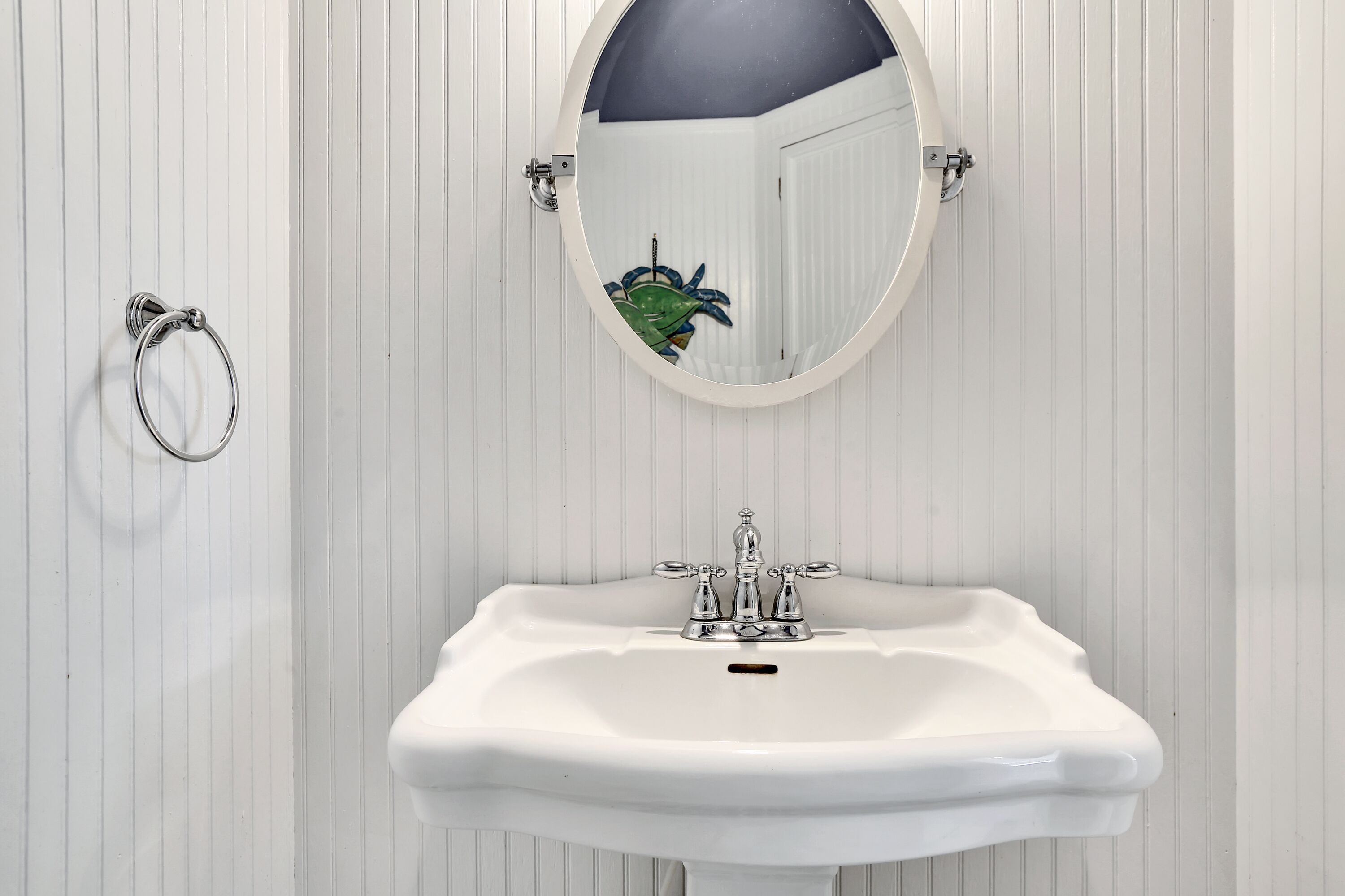Un baño con un lavamanos blanco, un espejo redondo y un aro para toallas.
