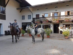 Two horses with riders in front of a building with a balcony and potted plants. - Ferienwohnung 2 im Dachgeschoss für 2 - 4 Personen,  70 qm, mit 2 sep. Schlafzimmern (Grabenstätt)