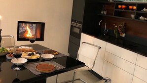 Una cocina moderna con una mesa de comedor dispuesta para una comida, un televisor mostrando un fuego, y una encimera con diversos objetos.