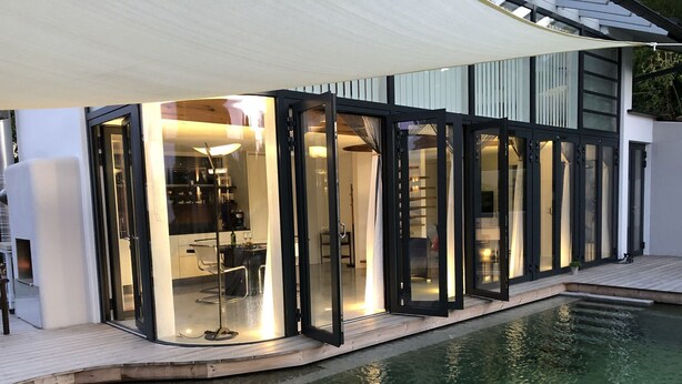 Una casa moderna con piscina, que cuenta con un patio cubierto de cristal donde se puede ver una cocina en el interior.