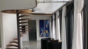 Un interior moderno con una escalera espiral, asientos redondos negros y pinturas abstractas.