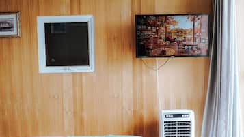 Quarto de hotel com parede revestida em madeira, televisão fixada acima de uma janela e ar condicionado portátil.