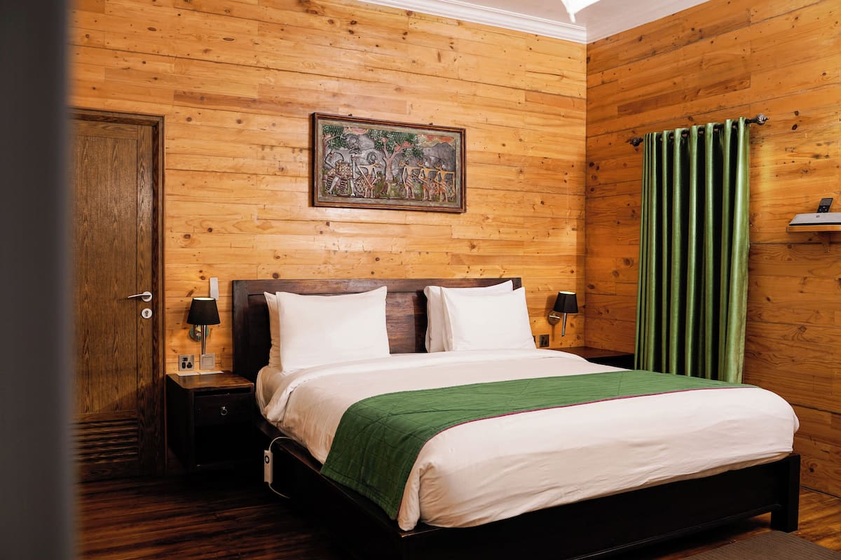 Una habitación con paneles de madera, una cama, una mesita de noche, una lámpara y un cuadro en la pared.