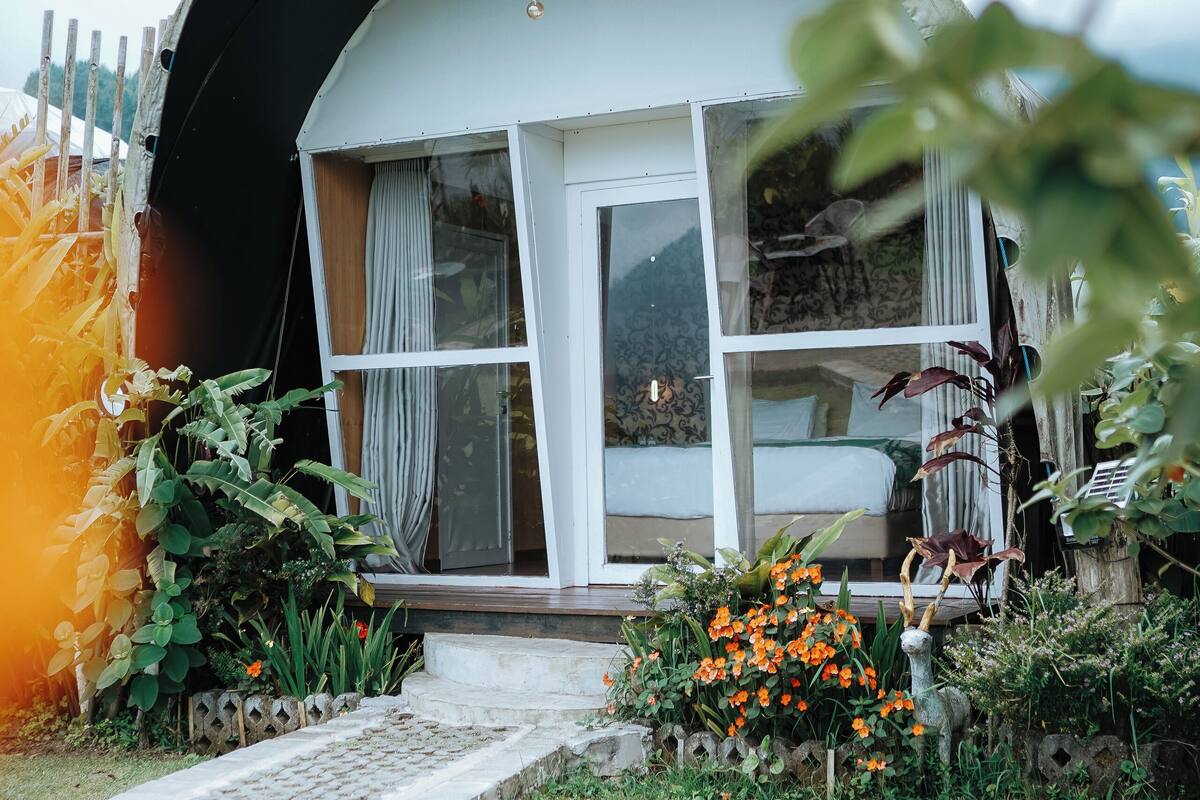 Una casa con techo curvo, un porche con banco y un jardín lleno de flores y plantas.