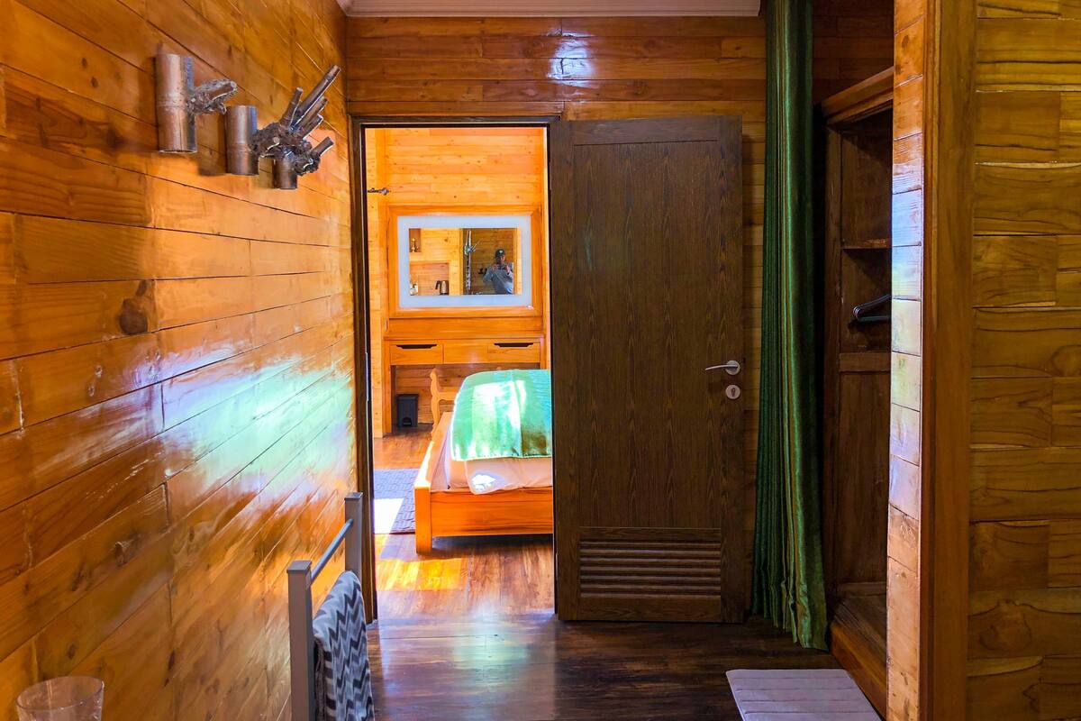 Un pasillo interior de madera que conduce a un dormitorio con cama, espejo y puerta.
