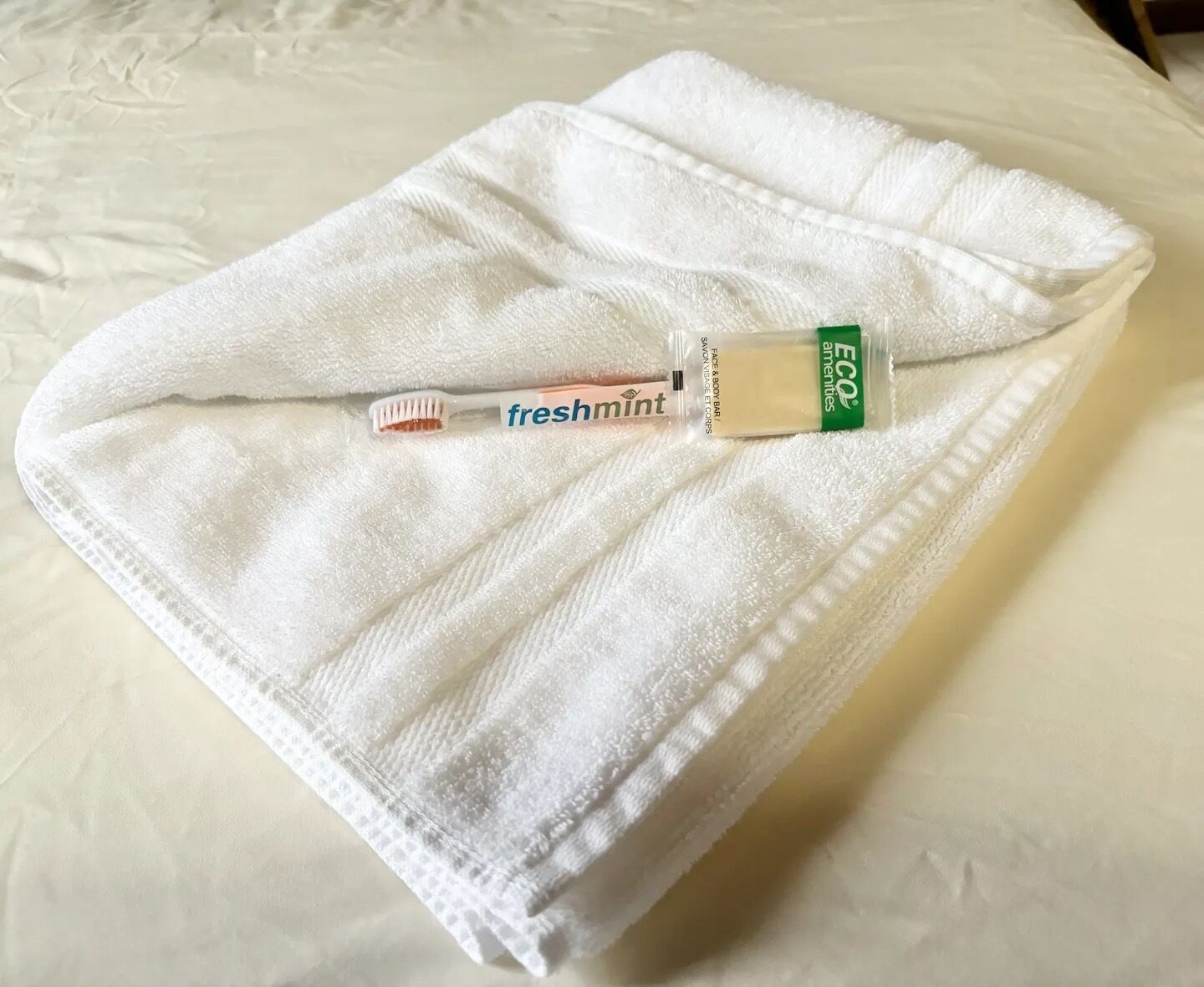 A white towel on a bed with a toothbrush and a tube of toothpaste.