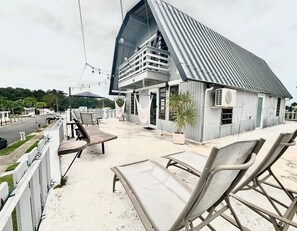 Una propiedad frente a la playa con asientos al aire libre, un edificio grande con techo inclinado y vistas a la calle y la vegetación.