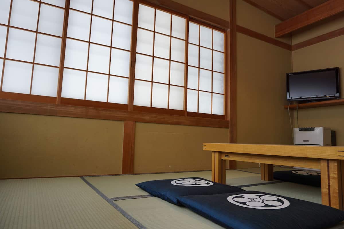 A traditional Japanese room with tatami flooring, a shoji screen, a television, and a small table.