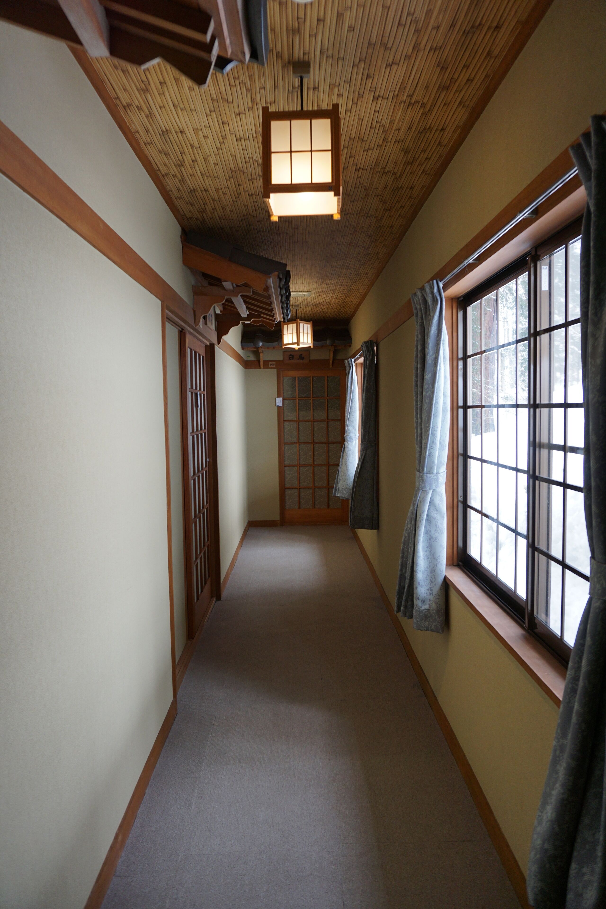 A narrow hallway with tatami flooring, wooden beams, and a shoji screen door.