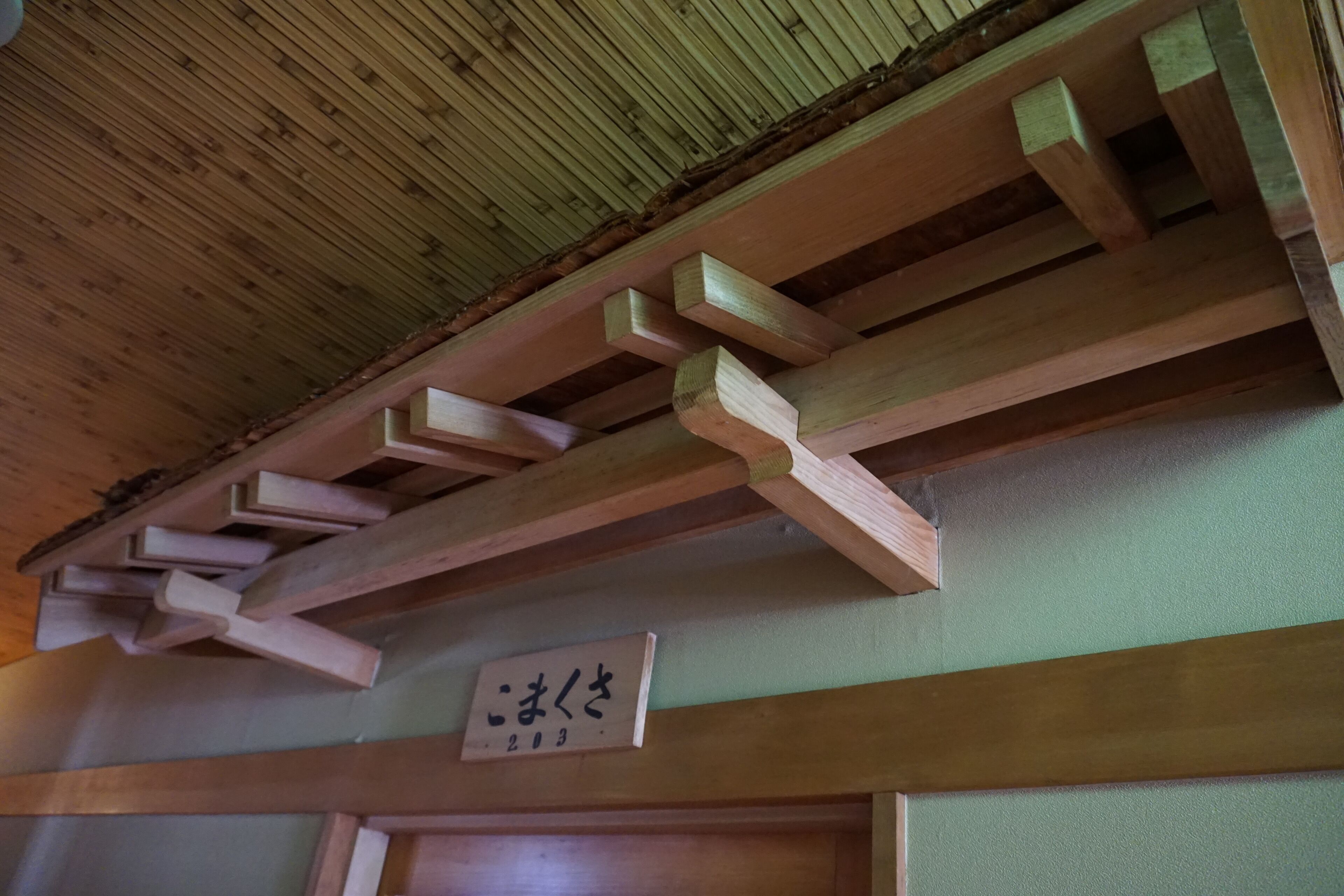 A wooden ceiling with a slatted design and a wooden beam structure. A sign with Japanese characters is visible on the wall.