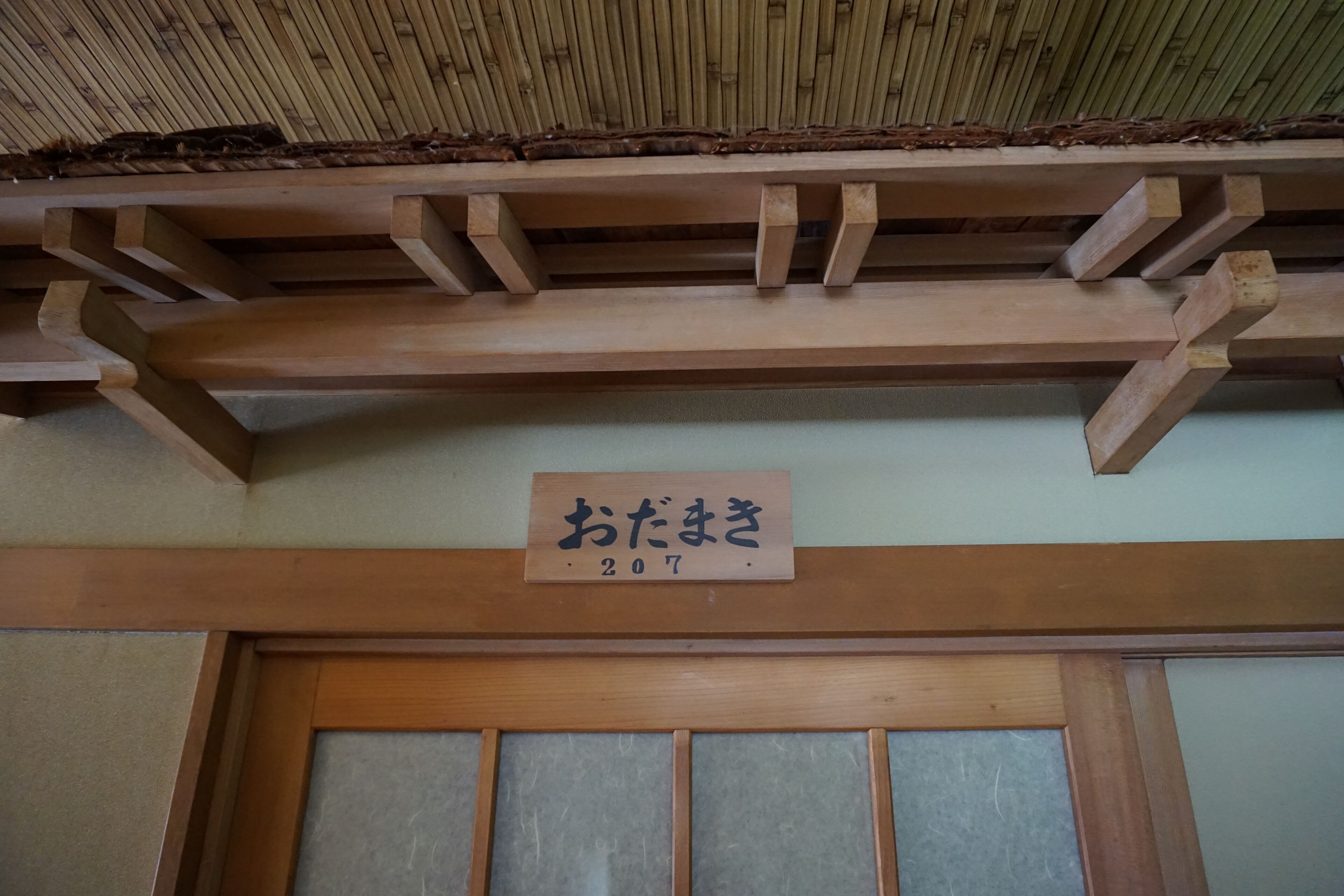 Techo de madera con textura similar al bambú y estructura de vigas. Se ve un letrero con caracteres japoneses y el número 207.