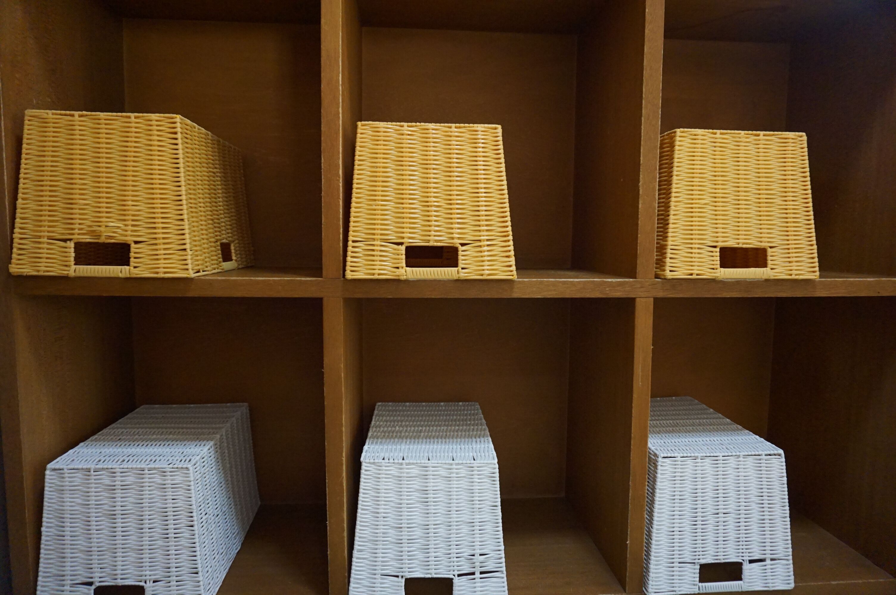 A wooden shelf with six wicker baskets, three on the top row and three on the bottom row.