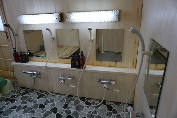Une salle de bain avec trois lavabos, chacun étant surmonté d’un miroir. On y trouve des flacons de produits de toilette sur le comptoir, et le sol est carrelé.