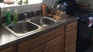 Une cuisine avec des meubles de rangement en bois, un évier en acier inoxydable, un four à micro-ondes et une fenêtre avec des jardinières sur le rebord.