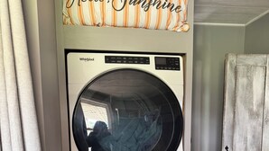 Un appareil combiné lave-linge et sèche-linge, avec une pancarte indiquant « Bonjour, soleil » placée au-dessus.