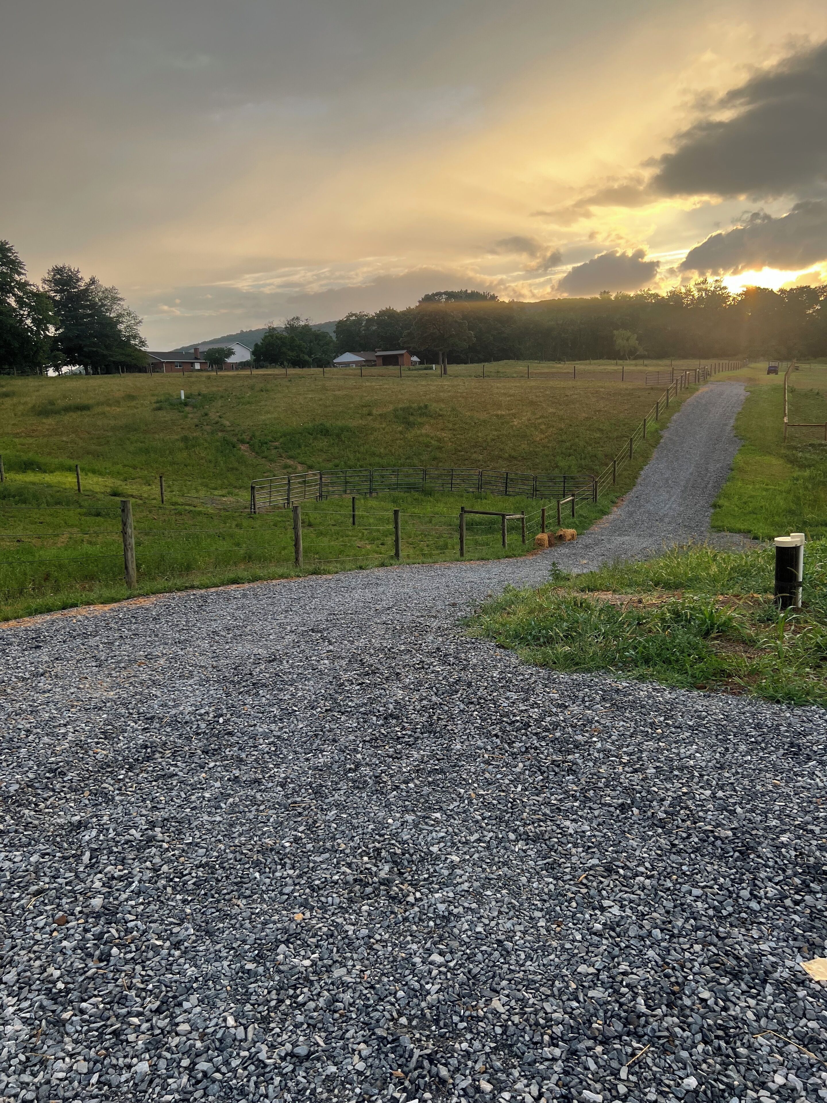 Un camino de grava serpentea por un campo cercado, con una casa de campo al fondo.