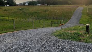 Un camino de grava serpentea por un campo cercado, con una casa de campo al fondo.