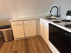 Una cocina con armarios blancos, un bote de basura de acero inoxidable, una estufa negra y un lavamanos con grifo.