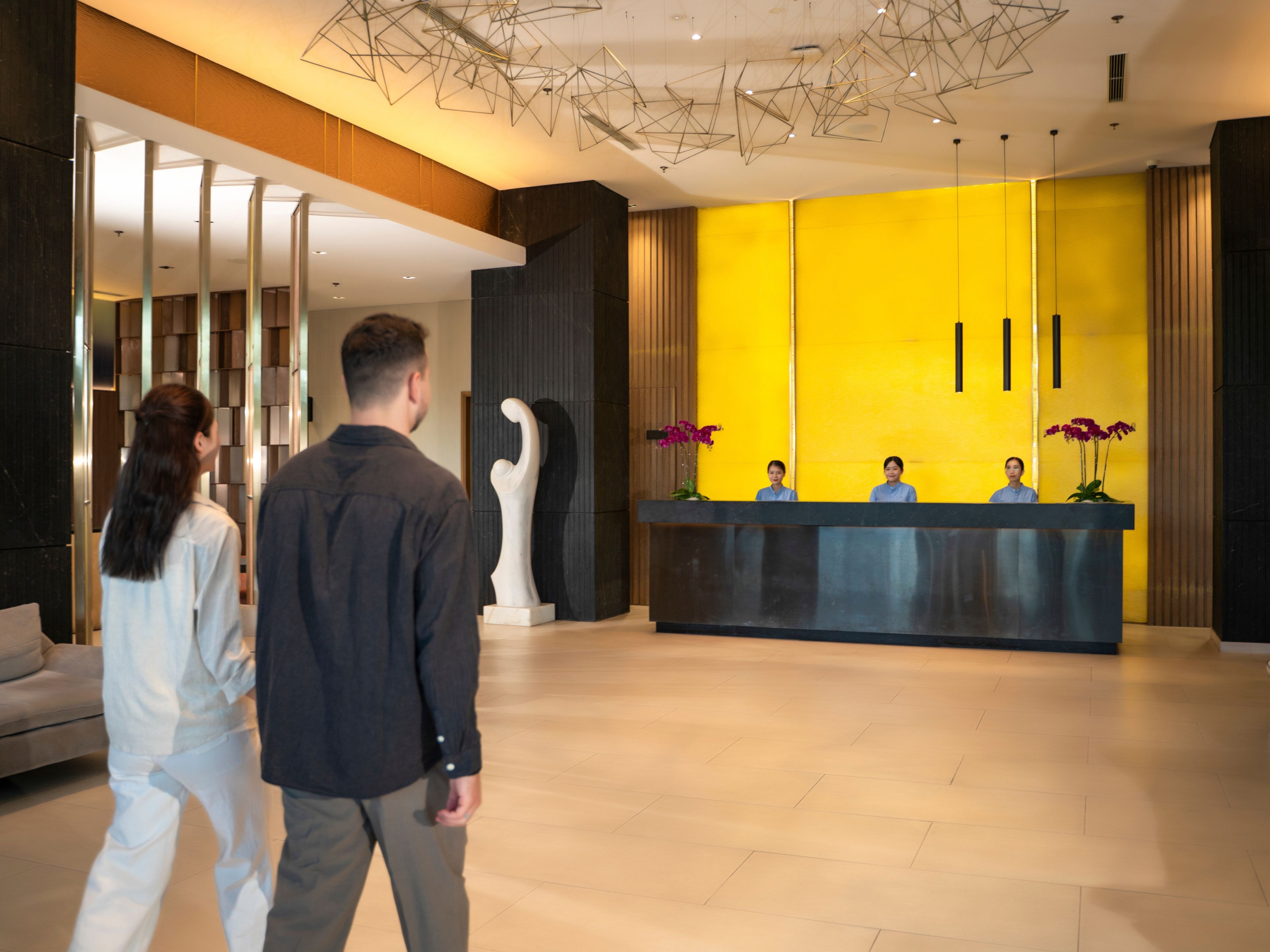 Zona d'arribada amb un disseny modern, que destaca un taulell de recepció, una gran paret groga i elements d'il·luminació contemporània.