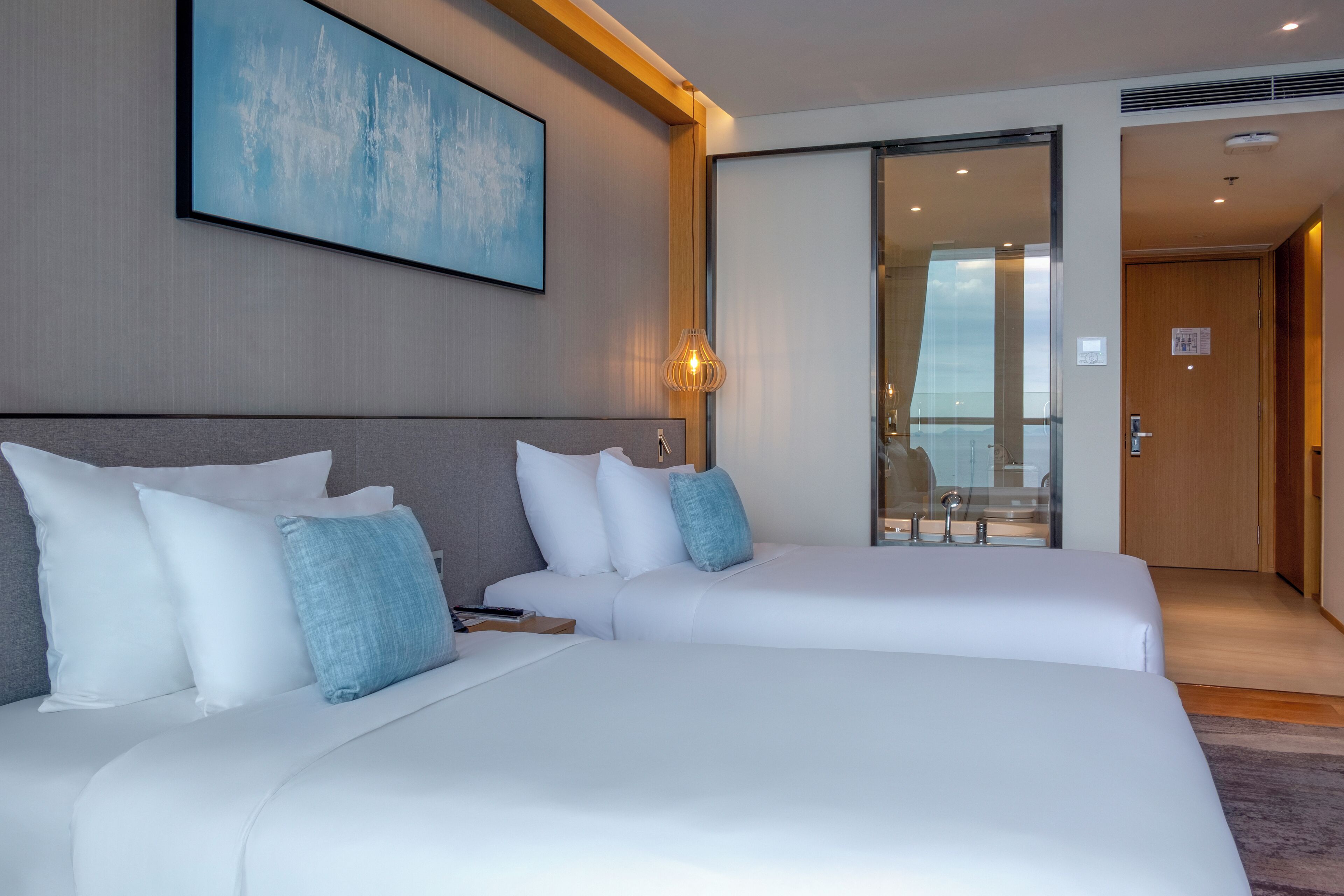 A hotel room with two beds, a large window, and a painting on the wall.