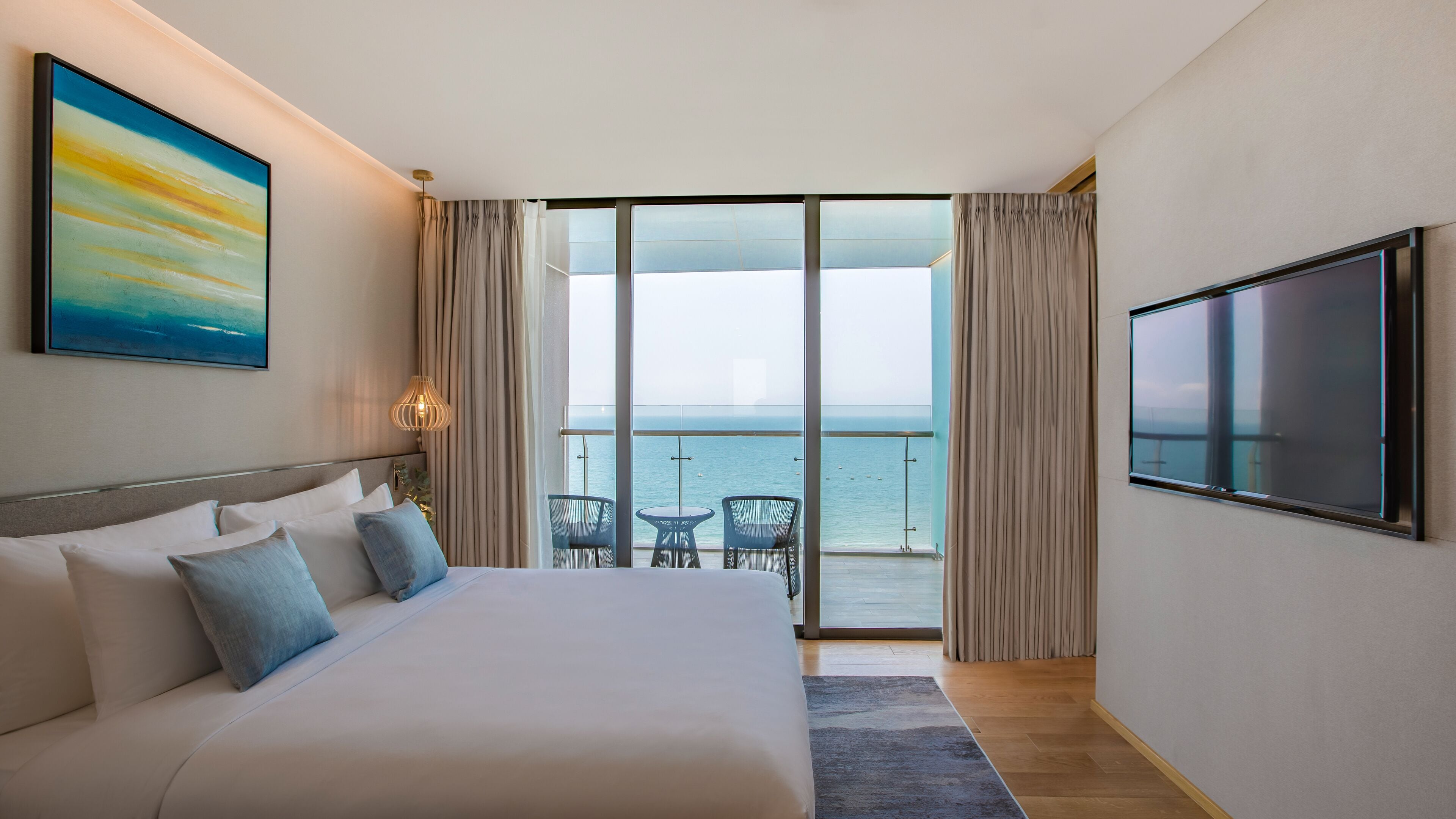 Une chambre d’hôtel avec un grand lit, une télévision, un tableau et un balcon donnant sur la mer.