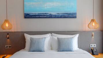 Hotelkamer met een groot bed, twee bedlampen, een schilderij van de oceaan en een telefoon op het nachtkastje.