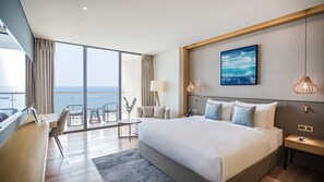 A hotel room with a large bed, a desk, a chair, a lamp, and a view of the ocean. - Prince Hotel Da Nang  (Da Nang)